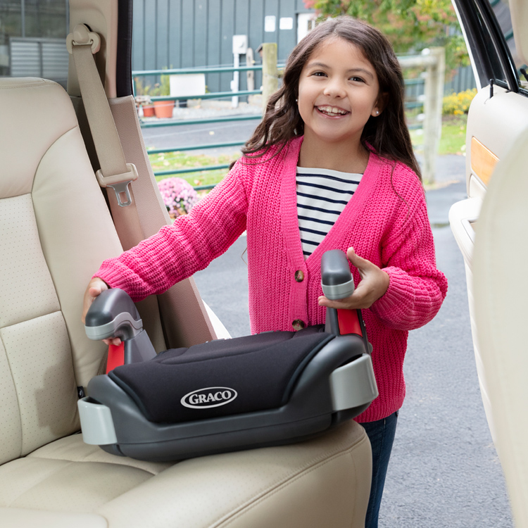 Young girl placing Graco's Booster Basic car seat in the car.