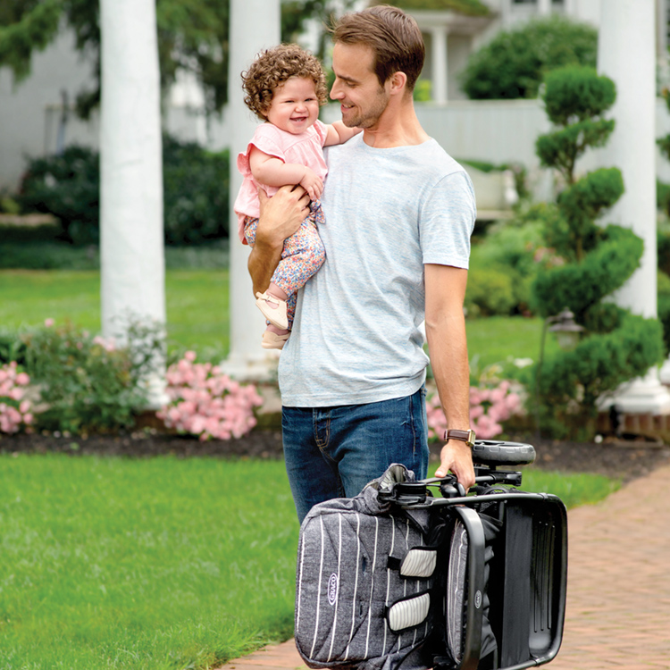 Dad carrying Graco Breaze Lite™ with one hand while holding his baby in the other