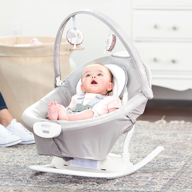Kleines Baby schaut auf die Spielzeugstange und entspannt in der abnehmbaren Wippe der elektrischen Babyschaukel Graco Duet Sway