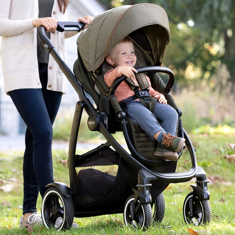 Mum pushing Graco® Evo® XT over grass as little boy rides in the pushchair