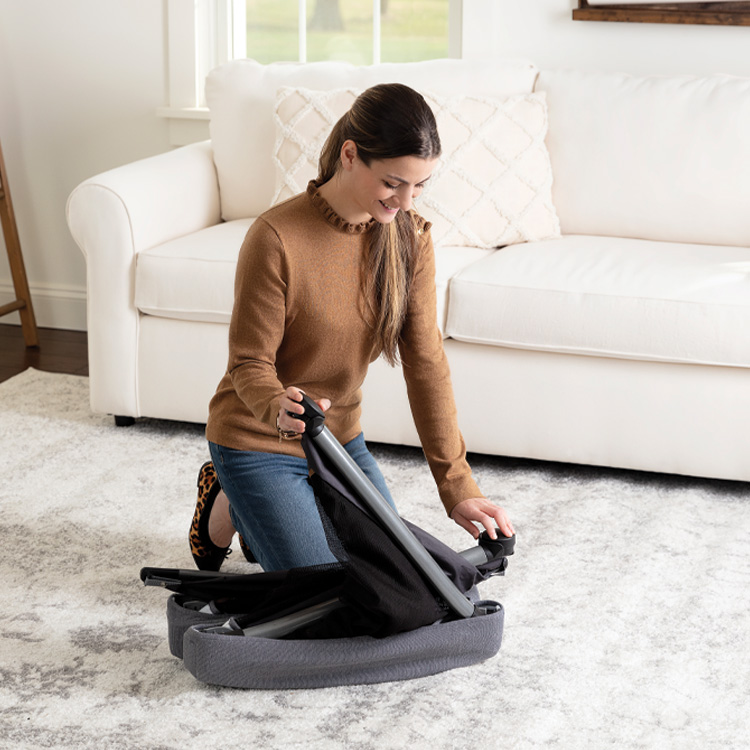 Mutter faltet das graue leichte Reisebett Graco FoldLite im Travel-Fold-Modus im Wohnzimmer