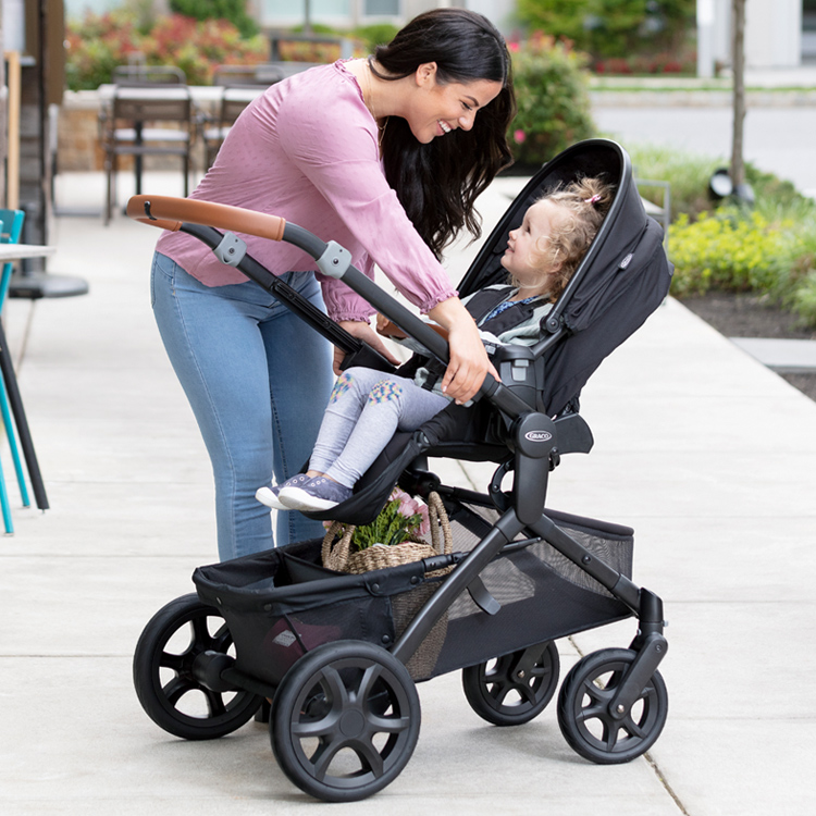 Mum sliding Graco Near2Me Elite pushchair seat closer to her while little girl sits in the seat