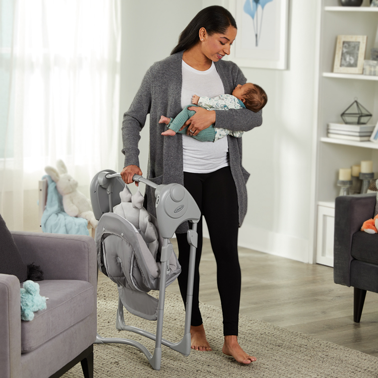 Woman holding baby in one arm and carrying Graco Slim Spaces in other hand
